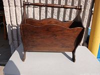 Overall angled view of the wooden magazine rack showing the sides, handle, and legs.