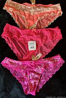 Three Victoria's Secret lace panties displayed on black background, showing color and lace details.