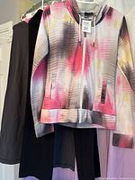 Front view of the Bench hoodie with gradient pink, grey and white pattern, and two pairs of yoga pants hanging behind, one black and one grey.
