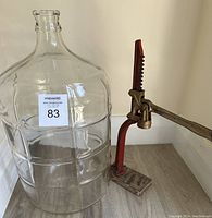 Photo showing the 5 gallon clear glass carboy with ribbed design alongside the floor corker.