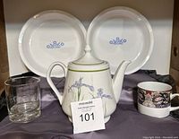 Photo showing two white CorningWare pie plates with blue cornflower designs, Shadow Iris teapot, ceramic mug, and glass tumbler arranged on a surface.