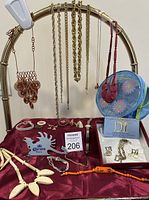 Photo showing wide range of costume jewelry pieces laid out on a burgundy cloth with a blue floral cosmetic bag and Caravelle by Bulova watch displayed