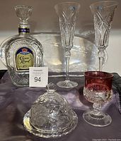 Lot of crystal and glassware items displayed together: Crown Royal 15 decanter, two crystal wine glasses, cranberry crystal goblet, butter dish, and fish plate.