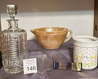 Full view of all four items: crystal decanter with stopper, orange glass mixing bowl, ceramic container, and boxed cake server.
