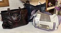 Three purses displayed on counter: burgundy Danier leather purse with crocodile pattern and lock detail, purple and white Guess purse with Guess plaque, blue suede Guess purse with silver studs.