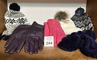 Three winter hats in black/white patterns and white with fur pom-pom, pairs of mittens in pink knit and blue fuzzy fabric, and one pair of purple leather gloves.