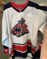 Front view showing larger embroidered Columbus Blue Jackets older logo in red, white, navy blue with stars, red collar and striped cuffs.