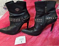 Side view of the black Harley Davidson ladies boots showing studded strap and logo, with pointed toe and stiletto heel.