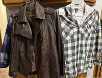 Overall view of three garments: brown Guess leather jacket in front, purple winter coat behind, black-and-white plaid Eddie Bauer shirt on the right