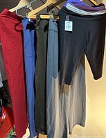 Five pairs of pants hanging on a rack showing various colors and styles including red, blue, black and grey colored pants.