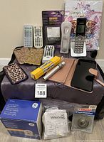 Lot of items arranged including remotes, phone cases, cordless phone, battery, thermostat and other miscellaneous electronics.