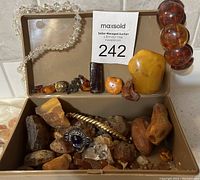 Open box showing assorted raw and polished amber stones, ring, chain and bracelets