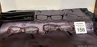 Four pairs of reading glasses displayed on a black cloth with a hard eyeglasses case and soft pouch.