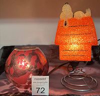 Photo showing both lights on a table with power cords visible. Snoopy light lit up with orange glow, round IKEA light also illuminated purple tone.
