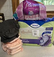 Photo showing Poise pads in long length, Tena Intimates overnight pads pack, and multiple Silhouette briefs in size medium stacked together.
