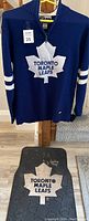 Blue and white knitted Toronto Maple Leafs adult small sweater hung on hanger with visible half zipper and front logo.