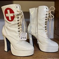 Front and side view of white patented leather high-heeled nurse boots with red cross emblem, lace-up front and platform soles.