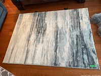 Large abstract patterned area rug with soft blend of gray, beige, and blue tones on the floor.