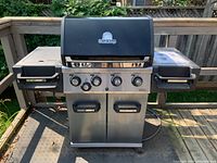Front view of Broil King grill on deck, showing hood, control knobs, cart and wheels