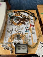 Overview of assorted jewelry laid out on tabletop, showing necklaces, bracelets, earrings, rings, cufflinks and pins