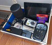 Overview of contents showing Amazon Echo speaker, Sony CyberShot camera, Insignia digital frame, chargers, battery, remote and film processing kit