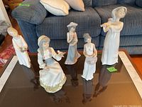 Five porcelain figurines arranged on a glass coffee table.
