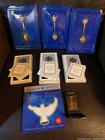 Photo of three sterling silver souvenir spoons in blue display cases, three Franklin Mint commemorative medals with certificates, Zippo lighter in box, and York souvenir pin packaging