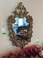 Full view of mirror mounted on wall showing the ornate gilded composite frame and reflective glass surface.