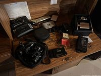 Wide top-down image showing the lot's items arranged on a wooden surface including Walkman, cassette player, binoculars in case, Polaroid camera, and clocks.