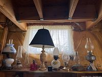 Wide view of nine lamps including glass chimneys and diverse bases behind a basement window
