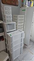 Multiple stacked white plastic storage organizers next to a tall white laminate cabinet with a door.