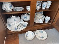 Cabinet view showing shelves with china, stacked plates, bowls, mugs and serving pieces