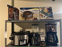 Photo showing Crockpot slow cooker, Oster blender, Cuisinart coffee maker, Rival fondue pot box, Winsome Wood marble cheese board box arranged on metal shelving