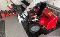 Side view of snowblower showing red housing, black engine, controls and wheels