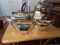 Group of four sterling silver pieces (tea pot, coffee pot, creamer, sugar bowl) on wood table