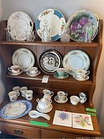 Full shelf showing assorted teacups, saucers, plates arranged with glass bottles and creamers