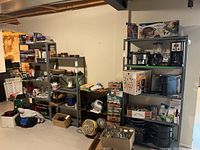 Photo showing three metal utility shelves arranged along a basement wall with various household items stored on them for display only