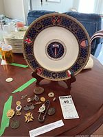 Overview of decorative plate on stand and assortment of pins and medals on table