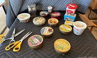 Overview of round tins with decorative labels and assorted buttons inside, with two pairs of yellow handled scissors