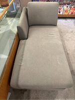 Full view of gray fabric chaise lounge showing cushioned seating area, backrest, and armrest with visible stains and wear.