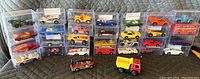 Overview of 24 collectible toy cars arranged closely together, mostly in clear plastic display cases with two without cases