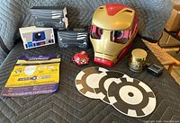 Iron Man mask, Star Wars themed boxes, Bluetooth speaker, red accessory, discs, mug, and cables arranged on padded surface.