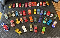 Top-down view of 38 collectible toy cars arranged on black quilted fabric, showing variety of styles, colors, and sizes.