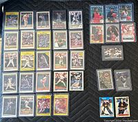 Photo showing 26 baseball cards and 7 basketball cards laid out on a dark surface. Cards are sleeved in plastic holders.