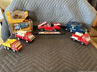 Group shot of model vehicles including boxed loaders and trucks, red Shelby Cobra, SWAT toy vehicle, and fire trucks arranged on fabric background.