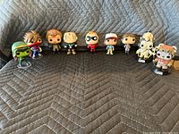 Nine collectible pop figures arranged in a line on a grey quilted surface