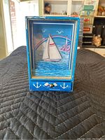 Front view of the music box showing the sailboat scene with moving waves and decorative drawer front.
