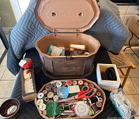 Open wooden sewing box showing the interior compartments filled with assorted sewing tools and supplies including thread spools, scissors, buttons, and pins.