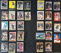 Top view photo showing an assortment of NHL, NBA, MLB, and NFL sports cards laid on a dark quilted surface, featuring Wayne Gretzky and other notable players.