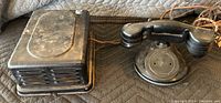 Top view of black antique telephone handset and separate speaker box on a padded surface